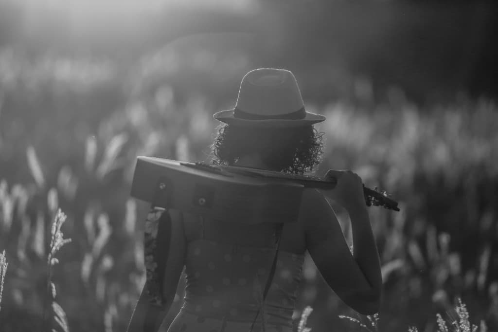 A musician carrying a guitar through a field